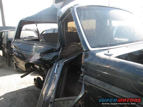 Dark SUV with crumpled roof and side, missing wheels, viewed from front-right