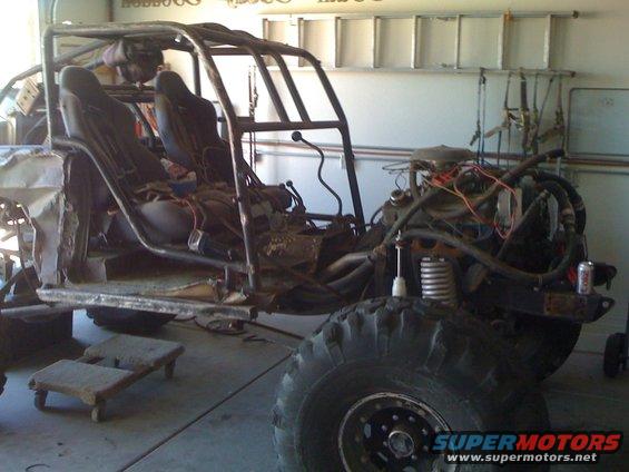 Custom buggy frame with engine, seats, and roll cage in a garage. Large tires are visible