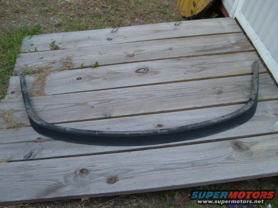 Black curved trim piece with visible screw holes, lying on wooden planks