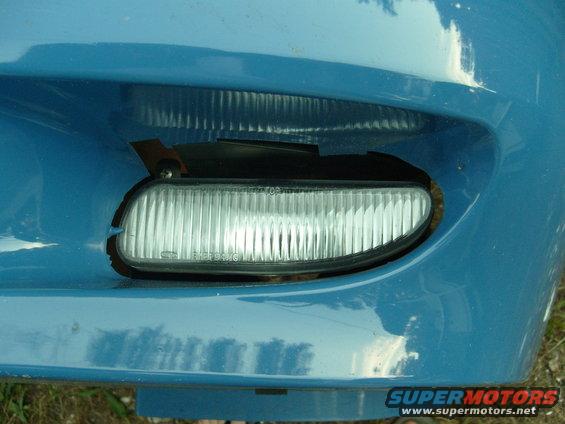 Blue car bumper with a clear fog light assembly, showing some damage and a SuperMotors.net watermark