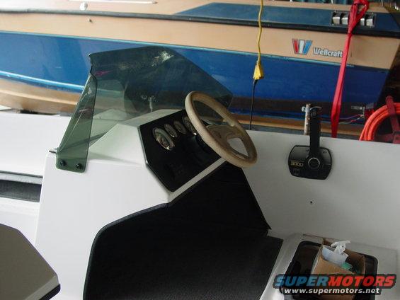 Boat interior with dashboard, steering wheel, and throttle control. A Wellcraft boat is visible in the background