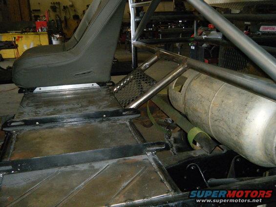 Off-road vehicle interior showing a bucket seat, roll cage, and large cylindrical fuel tank. Supermotors.net logo visible