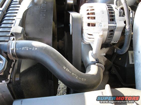 Close-up of engine bay showing radiator hose, alternator, and fan shroud with caution text