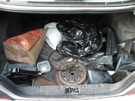 Car trunk interior with a jack, paper bag, black trash bag, and clutch assembly