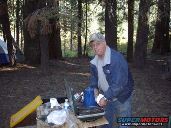 Man cooking at a campsite with tents in the background