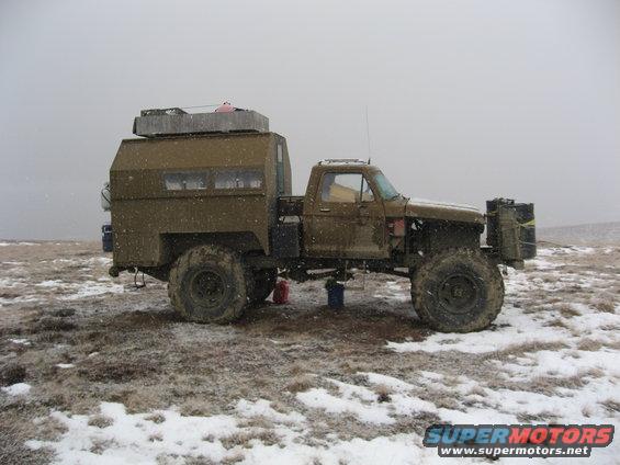 Olive green modified pickup truck with camper shell and large tires, side view