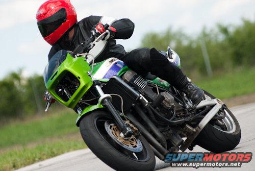 Motorcyclist in red helmet and black leathers leans hard into a turn on a green and white motorcycle