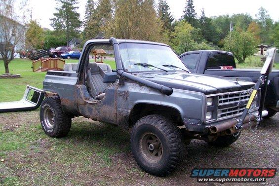 Off-road pickup truck with snorkel, removed doors, and custom bumper. Another truck is parked behind it