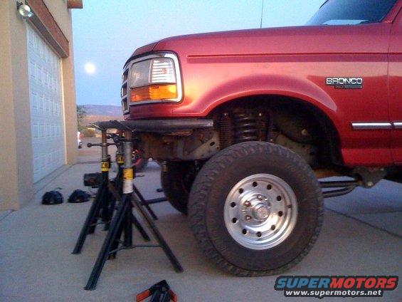 Red Ford Bronco on jack stands in front of a garage. Moon visible in the sky
