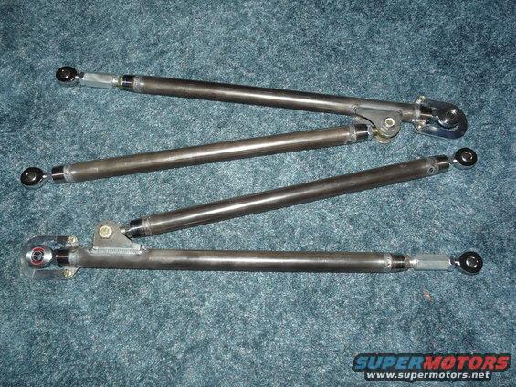 Four metal suspension control arms with threaded ends and spherical bearings, laid out on a blue carpeted surface