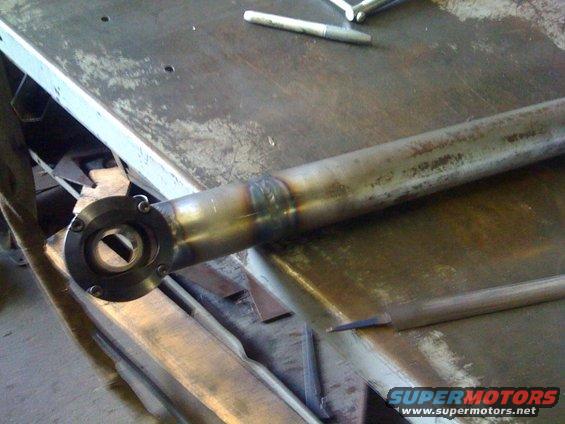 Welded metal tube with a flange on one end, resting on a workbench