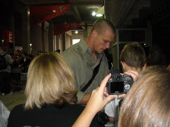 People gathered, one man signing autographs, another taking a photo with a digital camera