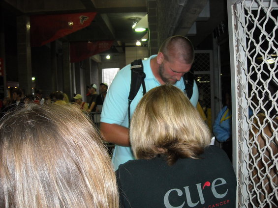 Man in light blue polo shirt with backpack signing autographs for people