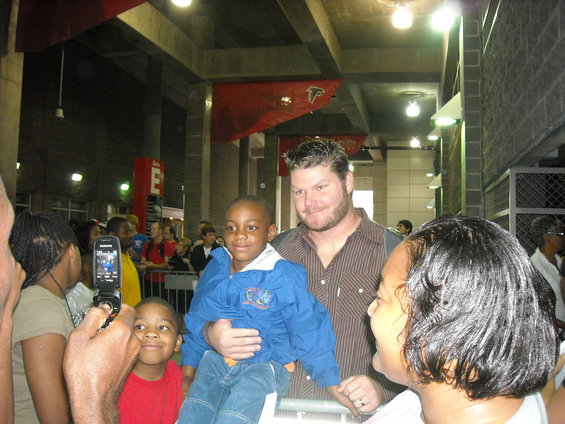 Man holding a child, with other people around. A flip phone is being used to take a picture