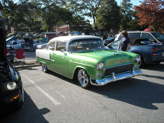 Green and white 1955 Chevrolet Bel Air parked at a car show. A black Mustang is partially visible on the left