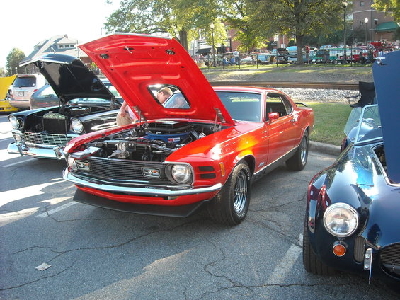 Red 1970 Ford Mustang Mach 1 with hood open, parked next to a black 1950s car and a blue Cobra