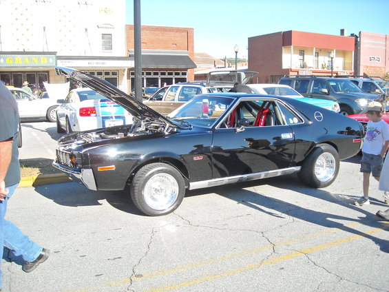 Black AMC Javelin with racing seats and roll cage, hood open. Other cars visible in background