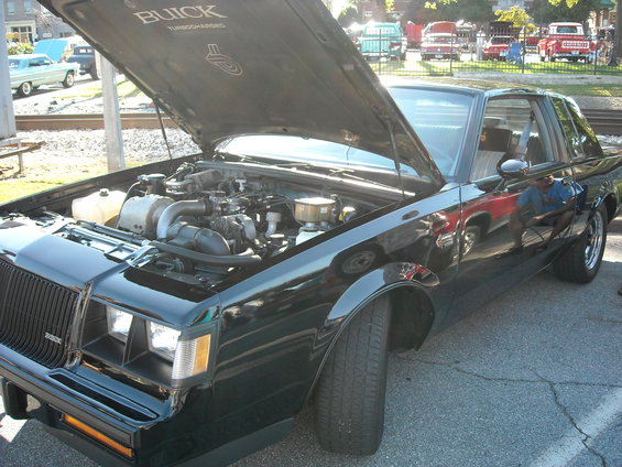 Black Buick Grand National with hood open showing engine. Other cars visible in background