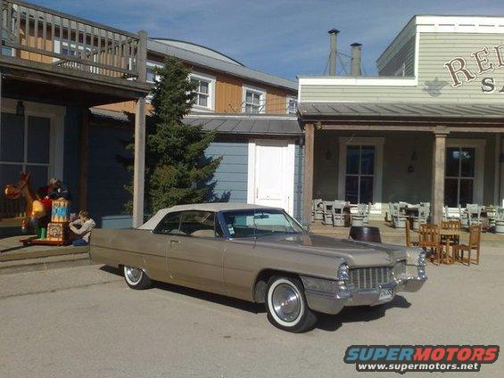 Tan 1969 Cadillac convertible parked in front of a building with a sign that says "RED S..."