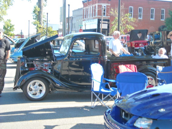 Black pickup truck with hood open, chrome wheels, and blue chairs nearby