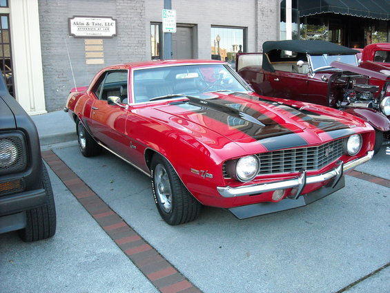 Red 1969 Chevrolet Camaro Z/28 with black stripes, parked next to other classic cars