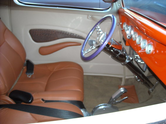 Interior view of a custom hot rod with tan leather seats, a purple steering wheel, and an orange dashboard with gauges