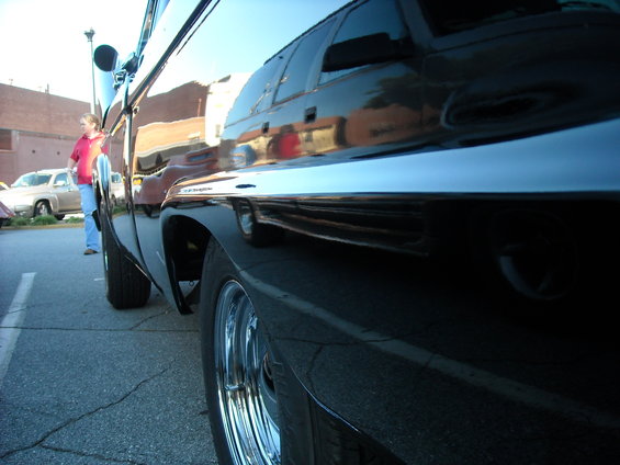 Black pickup truck side view, chrome trim, chrome wheels, reflection of buildings and people