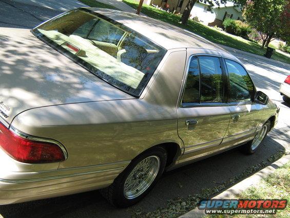 Tan Mercury Grand Marquis parked on a residential street, showing the rear passenger side