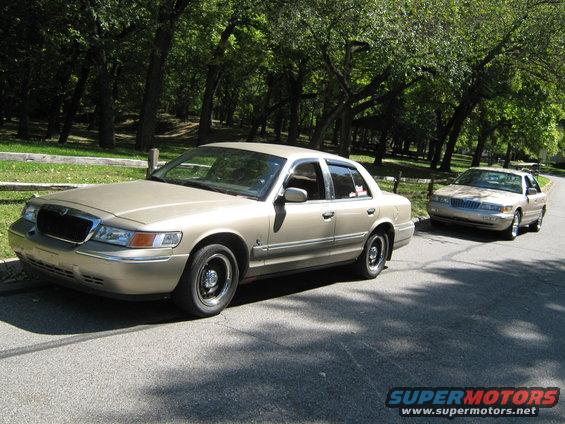 Gold 2000 Mercury Grand Marquis sedan parked on a road, with another identical car behind it