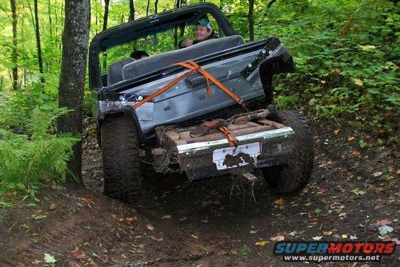 Jeep Wrangler with its rear end tilted up on a muddy trail, driver giving a thumbs up