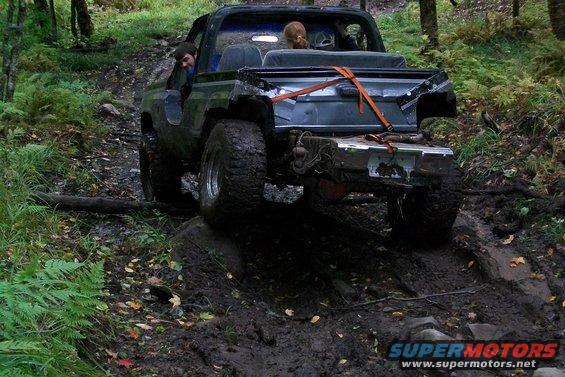 Black off-road SUV with large tires navigating a muddy trail, rear view