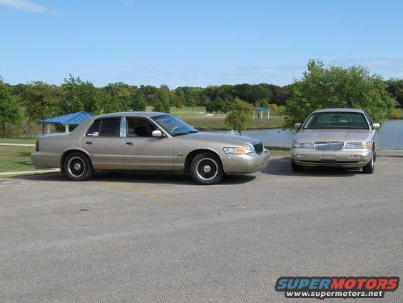 Two tan 2000 Mercury Grand Marquis sedans parked side-by-side on asphalt with trees and a lake in the background