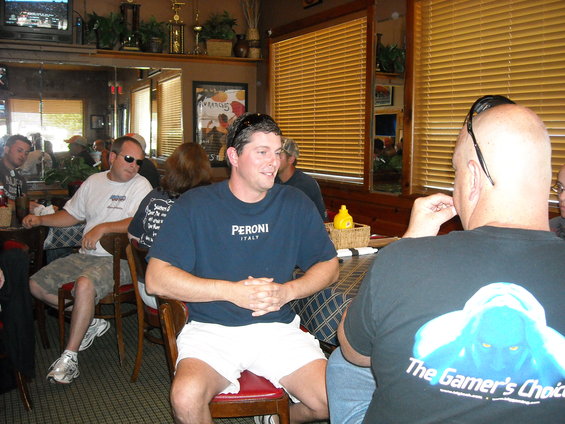 People sit at tables in a restaurant, with one man in a blue shirt with 'Peroni Italy' visible