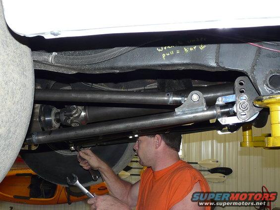 Undercarriage view of vehicle with driveshaft and suspension components. Man works on suspension