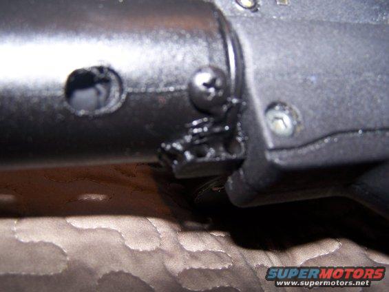 Close-up of a black plastic part with a screw and metal bracket attached, likely from a steering column