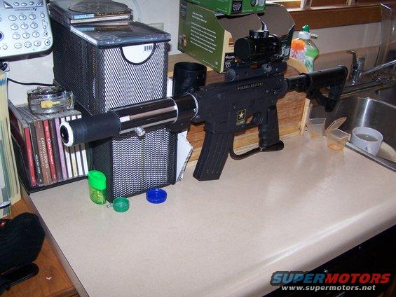 Assault rifle with scope and extended barrel on a counter next to CDs and a phone