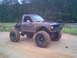 1984 Ford Bronco II - Modified pickup truck with oversized tires and a roll cage sits off-road.