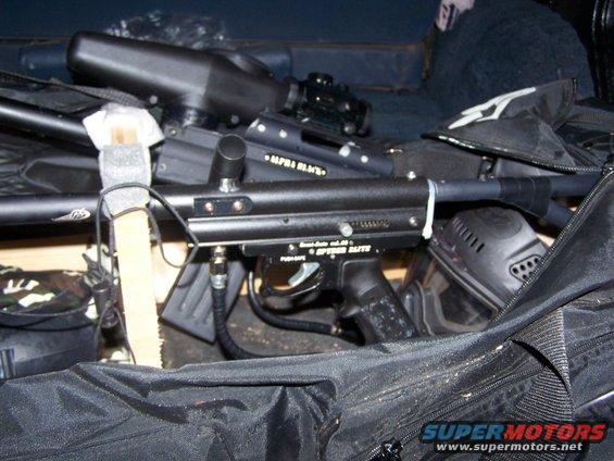 Paintball marker with "ALPHA BLACK" and "SPEEDER ELITE" visible, next to a mask and gear bag