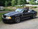 2000 Ford Excursion - A black convertible Mustang is parked on a gravel surface near a body of water with a fountain.