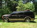 2000 Ford Excursion - A black Ford Excursion with tan accents and custom wheels is parked outdoors on a grassy area with trees.