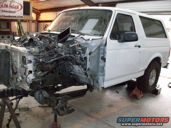 White Ford Bronco with front end disassembled, engine exposed, on jack stands