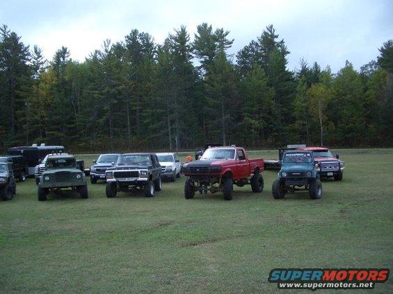 1994 Ford F-250 and other lifted trucks and SUVs parked on grass with trees in background
