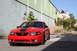 2004 Ford Mustang - A red 2004 Ford Mustang with black racing stripes is parked in front of an industrial building.