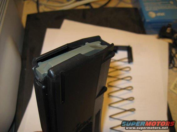 Black gun magazine with a gray follower and a coiled spring next to it