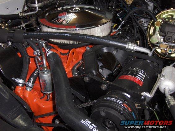 Close-up of a V8 engine with a chrome air cleaner showing a 396 badge. Orange block, black hoses, and AC compressor visible