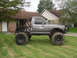 1984 Ford Bronco II - Modified 1984 Ford pickup truck with large off-road tires and a full roll cage is parked on a grassy lawn.