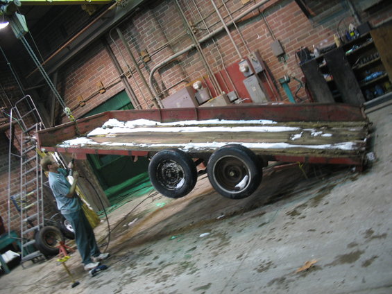 Trailer with wooden deck and red metal frame, being lifted by a chain hoist in a workshop