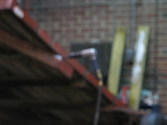 Close-up of red metal beams and a tool with a blue handle against a brick wall
