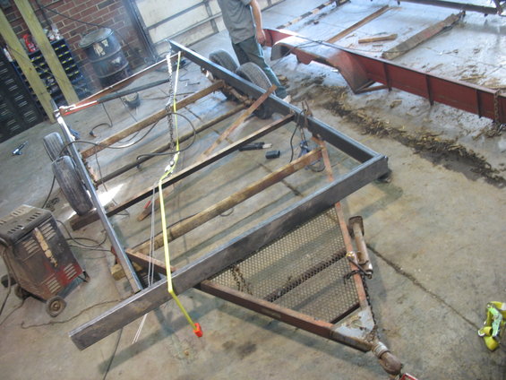 Trailer frame with two wheels, metal mesh deck, and tow hitch in a workshop