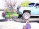 1900 Ford C-350 (Centurion Conversions) - A blue pickup truck is loaded onto a trailer, with a white truck visible in the background.